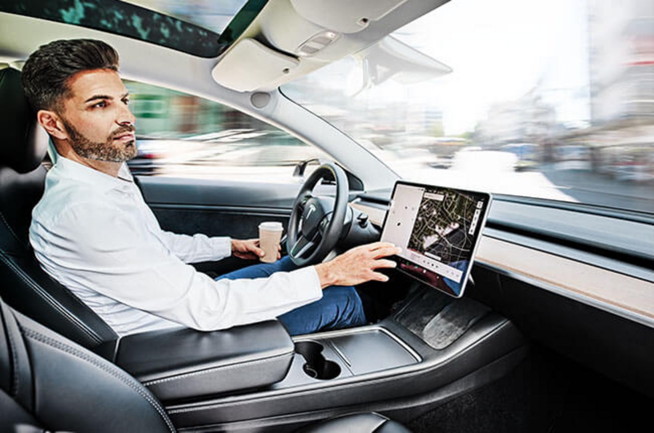 Das Bild zeigt einen jungen Mann wie er autonom in einem Tesla fährt.