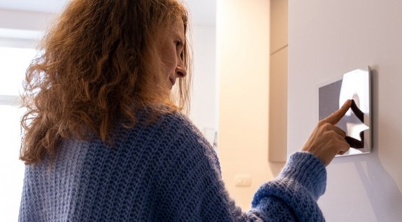 Frau tippt auf ein smartes Wandbedienfeld in einem modernen Raum.