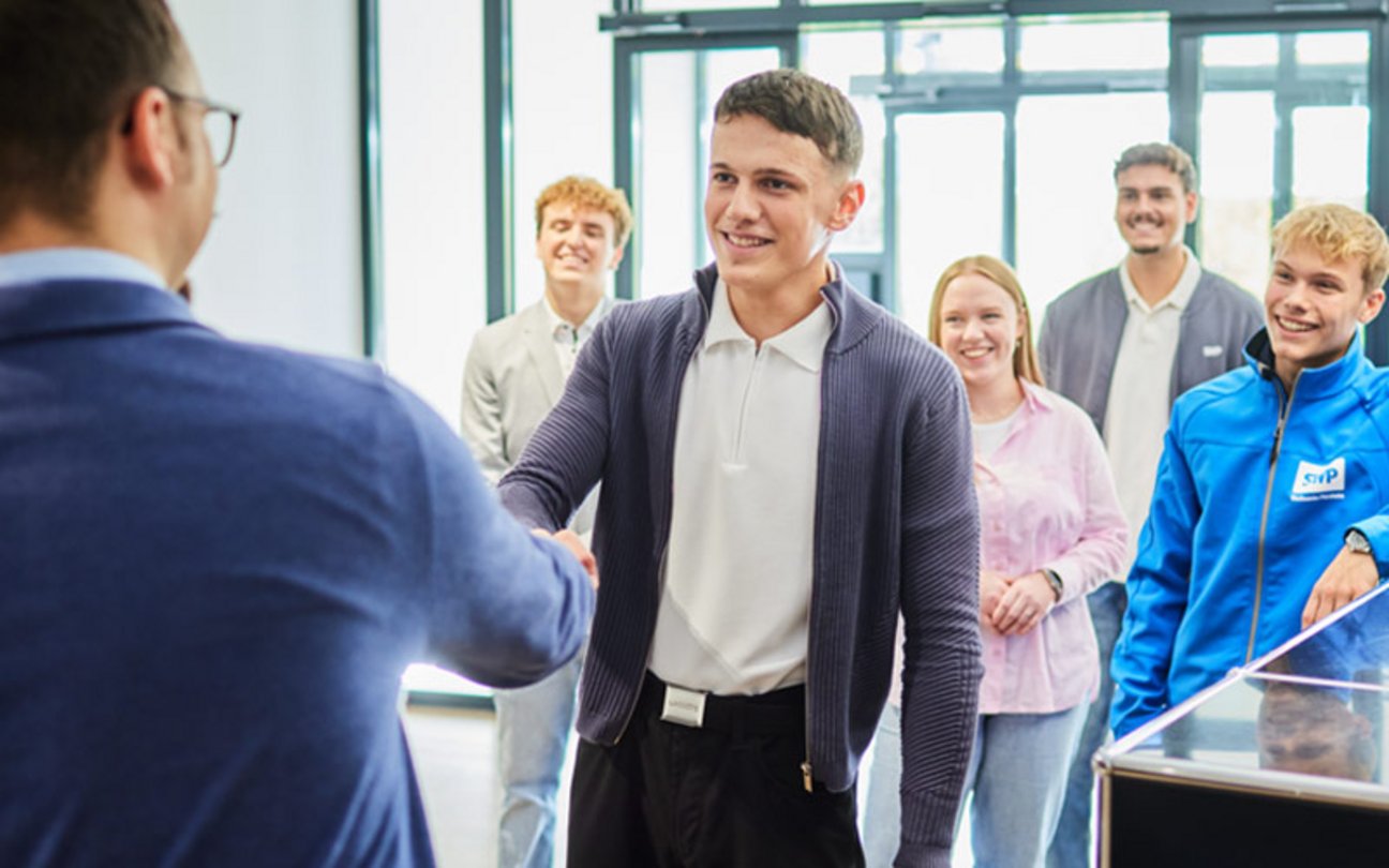 Junge Frau sitzt an einem Schreibtisch und arbeitet an einem Desktop-Computer in modernem, hellem Raum.