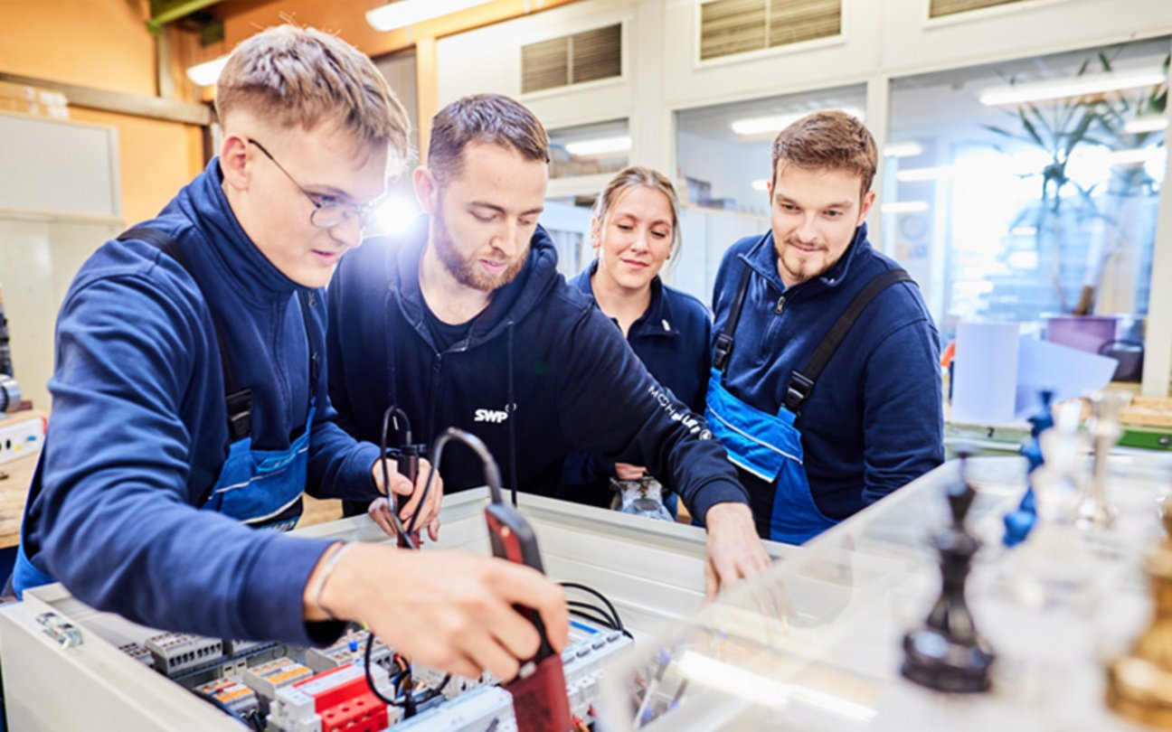 Das Bild zeigt Azubis mit Ausbilder, die mit elektrischen Geräten arbeiten.